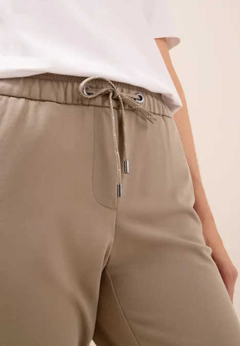 Nahaufnahme einer beige Jogginghose mit Kordelzug und weißem Oberteil.